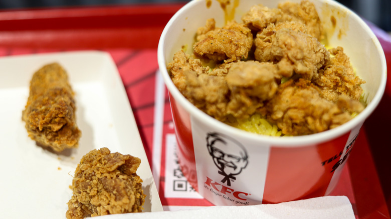 Kentucky Fried Chicken bucket, with two pieces of fried chicken on a tray beside it