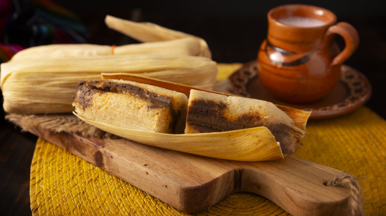 tamales resting on a cutting board, next to a mug filled with liquid