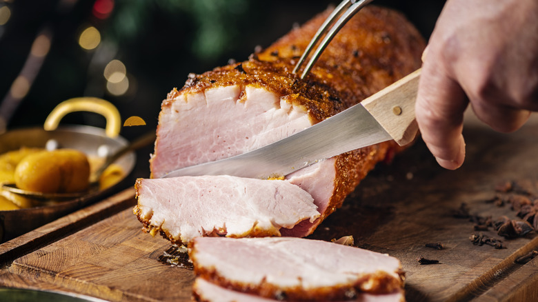 a hand slicing a Christmas ham