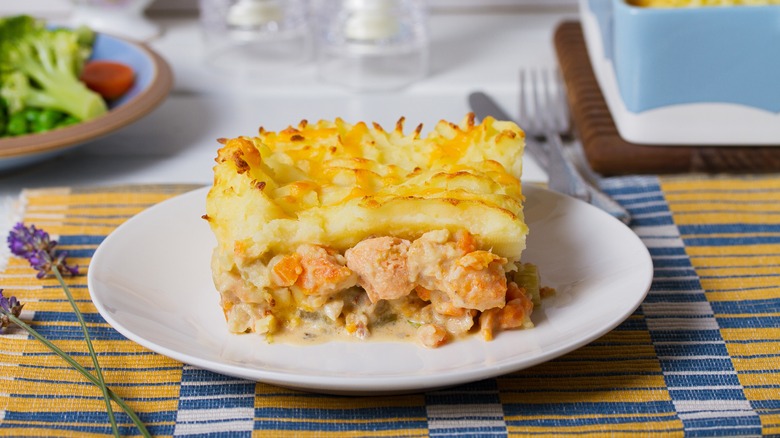 Slice of fish pie on a round white plate, with a sprig of lavender beside it