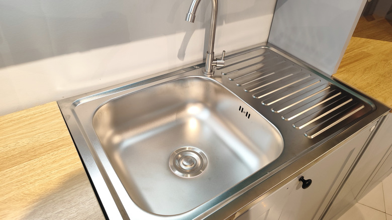 A stainless steel kitchen sink with a draining board and a stainless steel pipe