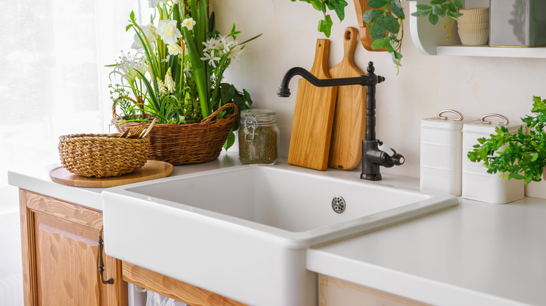 Bright kitchen with white farmhouse sink surrounded by greenery and wooden cabinets