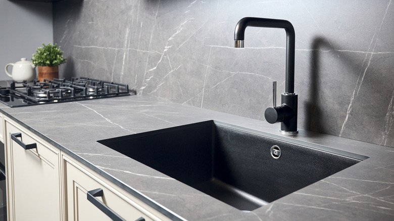 Detail shot of a single bowl kitchen sink with grey countertops and backsplash