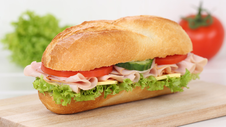 Hoagie roll filled with ham, cheese, and salad on a wooden cutting board