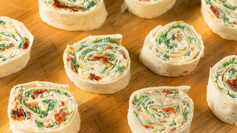 Cheese and spinach pinwheel sandwiches on wooden cutting board