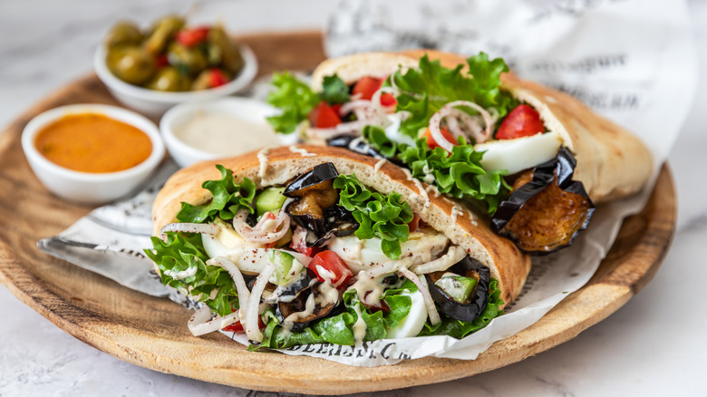 Pitas stuffed with roasted eggplant, eggs, and salad on a tray with sauces and garnishes