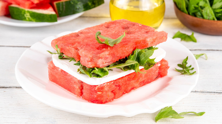Watermelon sandwich filled with cheese and arugula served on a white plate