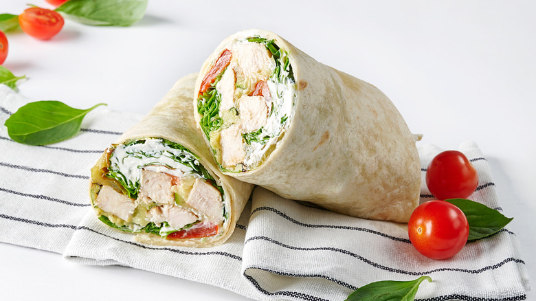Chicken salad wraps on stiped linen next to cherry tomatoes and basil leaves