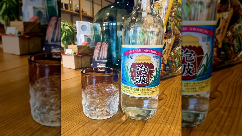 A bottle of awamori on a wooden table next to a glass at a restaurant.