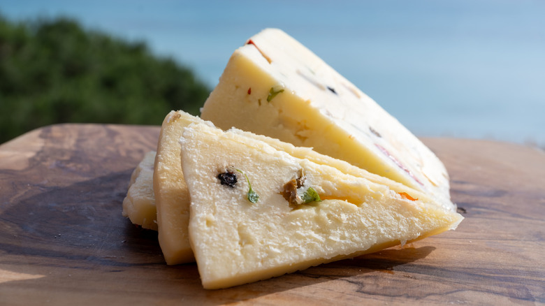 Sliced wedge of provolone on wooden cutting board with sea in background