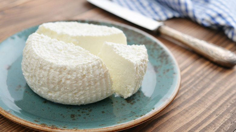 Round of ricotta on plate with knife in background