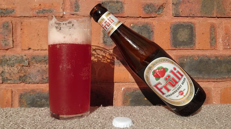 A bottle of Fruli Strawberry Beer resting on a glass filled with the beer on a sunny brick background