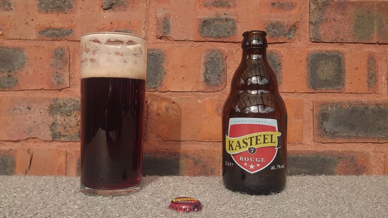 A bottle of Kasteel Rouge next to a glass full of the beer and the cap shown in front