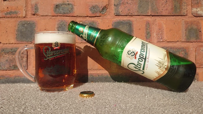 A bottle of Staropramen resting on a full branded glass with a red brick background