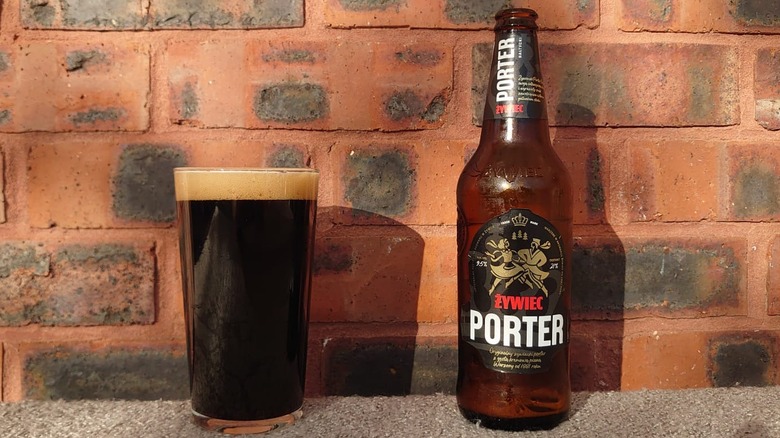 A bottle of Żywiec Porter in front of a sunny wall with a poured full glass by its side