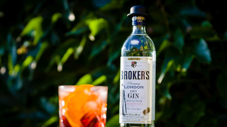 Bottle of Broker's next to a Negroni on a table outside.