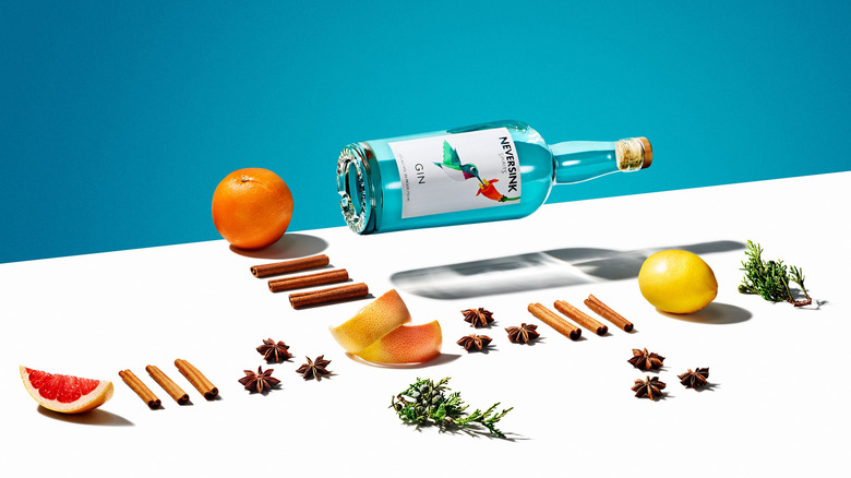 Bottle of Neversink Gin laid out next to meticulously set botanicals, herbs, and roots against blue and white background.