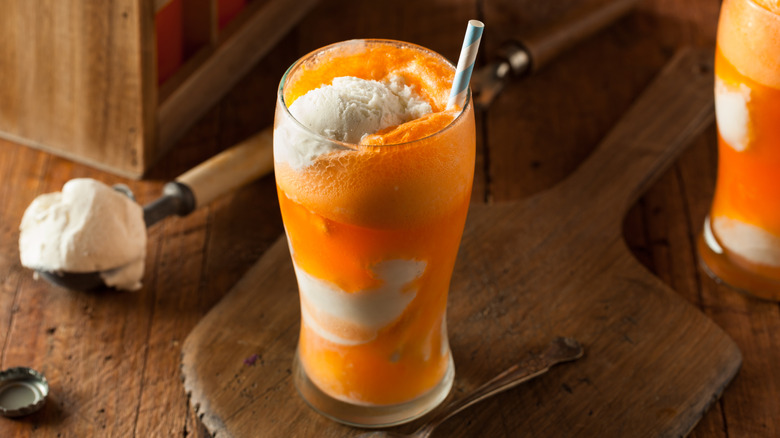 Orange soda ice cream float with straw and scoop of ice cream in background
