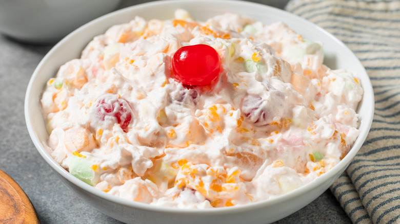 Ambrosia salad in white dish next to striped dish cloth on grey surface