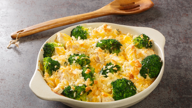 Chicken divan in round white casserole dish next to wooden spoon