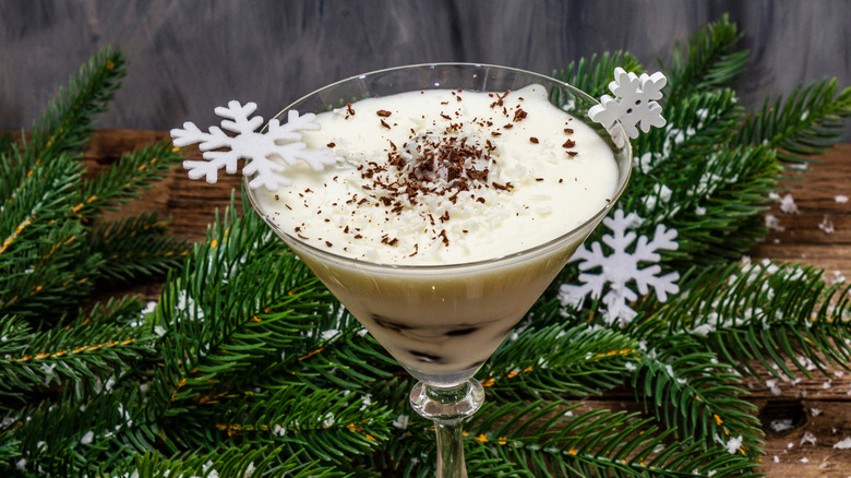 Prune dessert with walnuts and whipped sour cream with sugar in a martini glass decorated with snowflakes, green foliage in the background