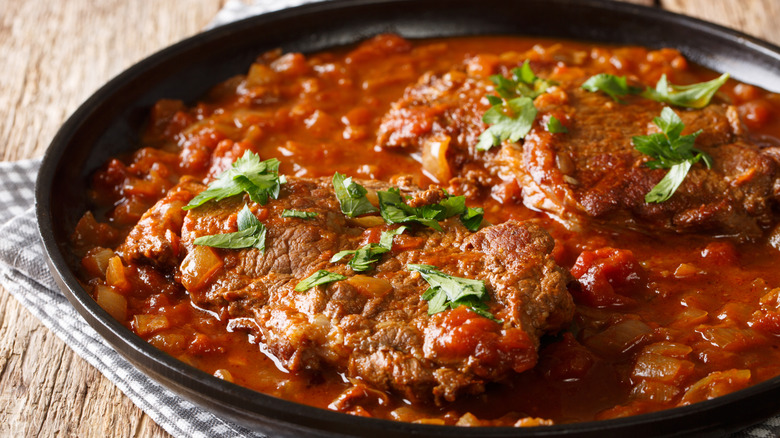 Black dish of Swiss steak on striped dish cloth and wooden table