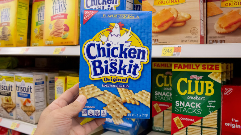 A person holds a box of Chicken in a Biskit in front of the cracker aisle of a grocery store.