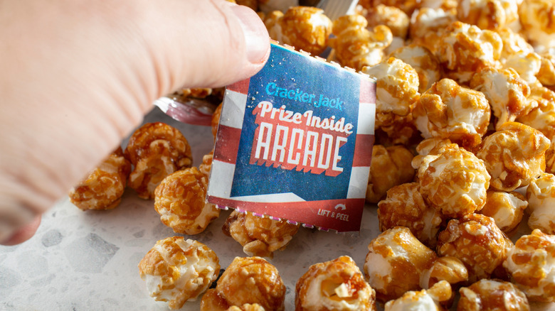 A person picks up the Cracker Jack prize sticker from a pile of cracker jack popcorn.