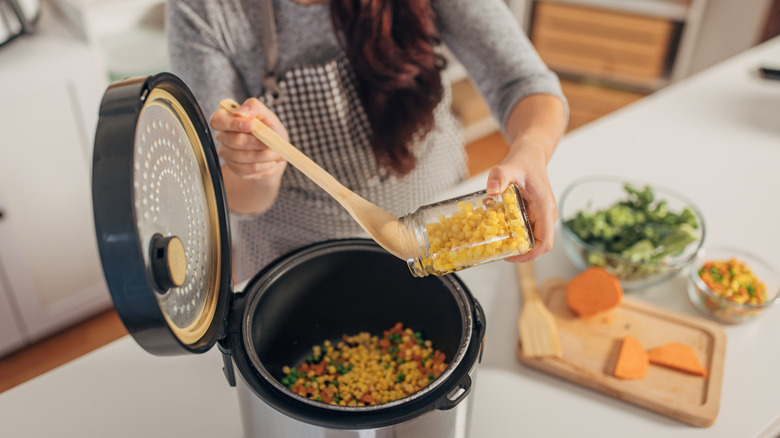 person spooning corn into a slow cooker on kitchen counter