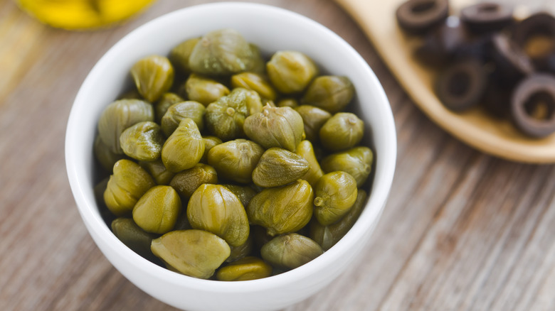 Capers in a white bowl on a wooden table