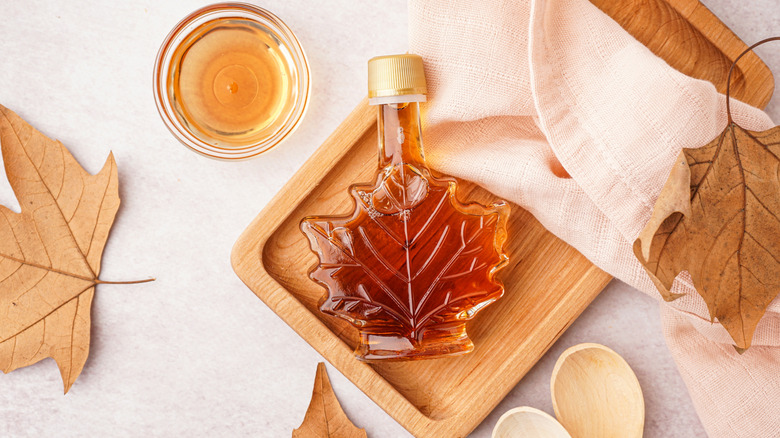 Maple syrup in a maple leaf bottle on a wooden cutting board