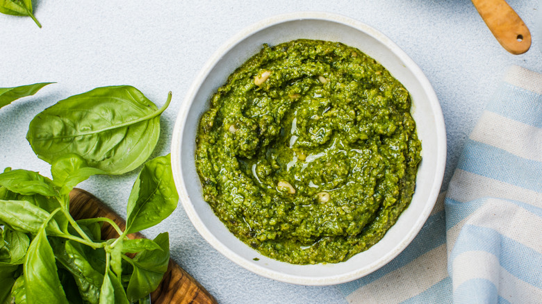 Pesto in a white bowl with basil on a grey table