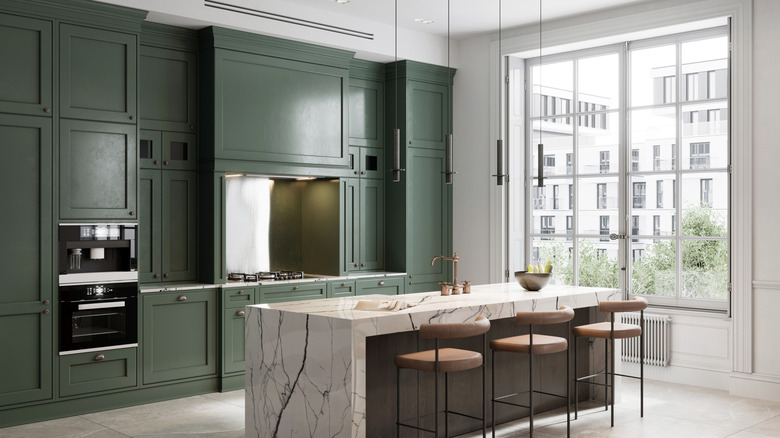 Kitchen with sage green cabinets, marble island, and large paneled window on the right