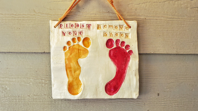 Sign that says "Please remove your shoes" with a child's foot prints.