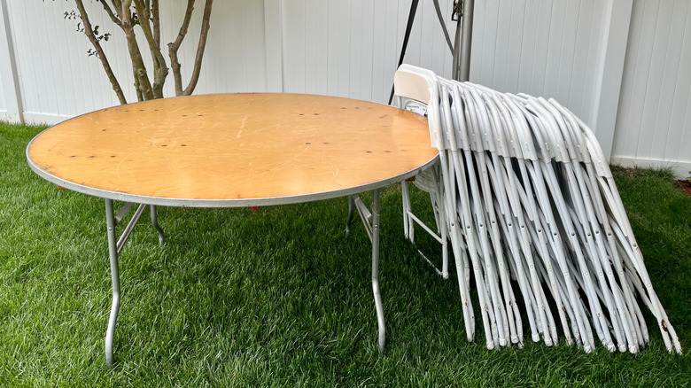 Folding chairs that are piled up on top of folding tables.