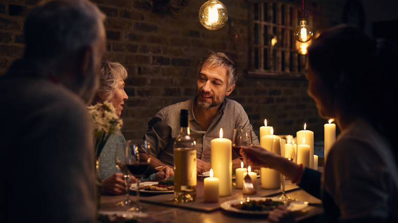 Group of people sitting in atmospheric dining room, with candles, drinking wine and eating food, relaxed family meal.