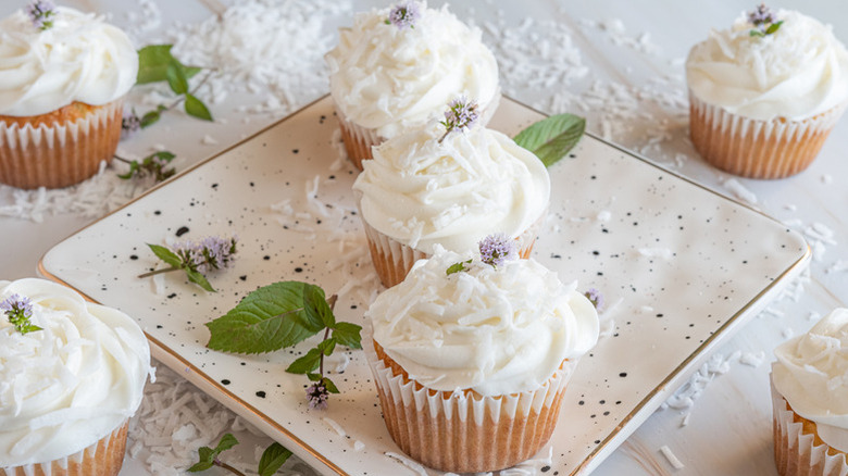 Plate of creamy coconut cupcakes, decorated with purple flowers