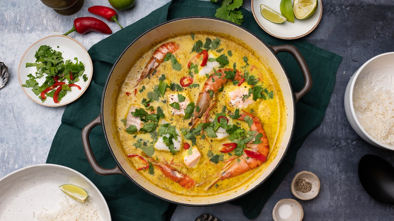 Seafood coconut curry in pot, topped with fresh cilantro and sliced chiles