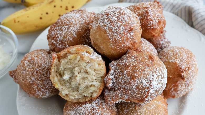 Pile of banana fritters on plate, dusted with powdered sugar