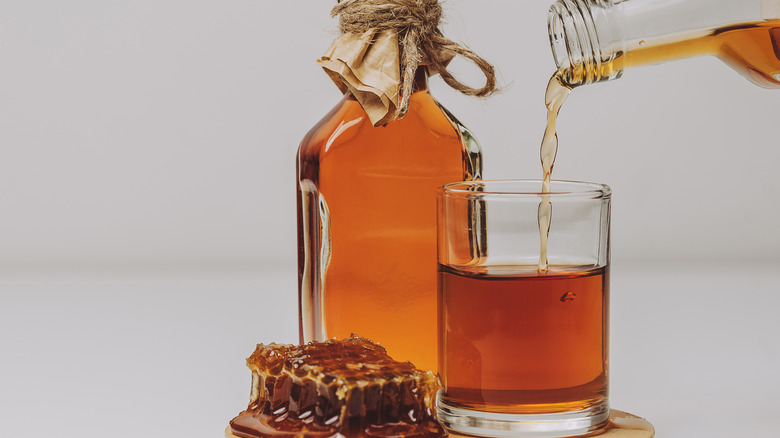 A bottle and tumbler of mead with honeycomb on the side