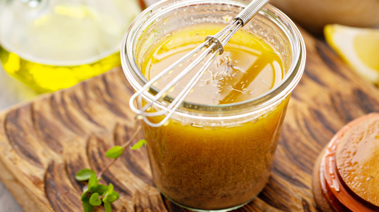 A jar of vinaigrette with a small whisk