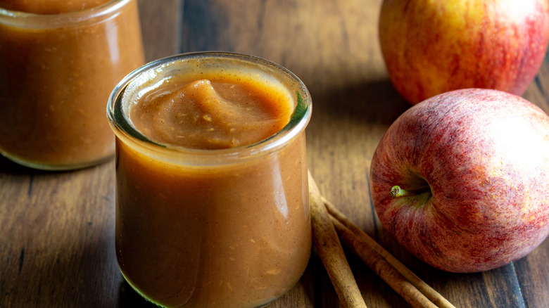 Jars of apple butter alongside a whole apple