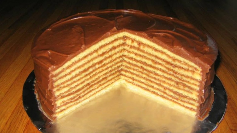 A Smith Island cake with a large slice cut out of it and a chocolate ganache topping