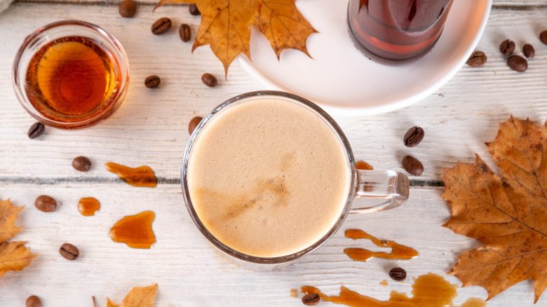 Maple syrup latte with coffee beans and leaves on table