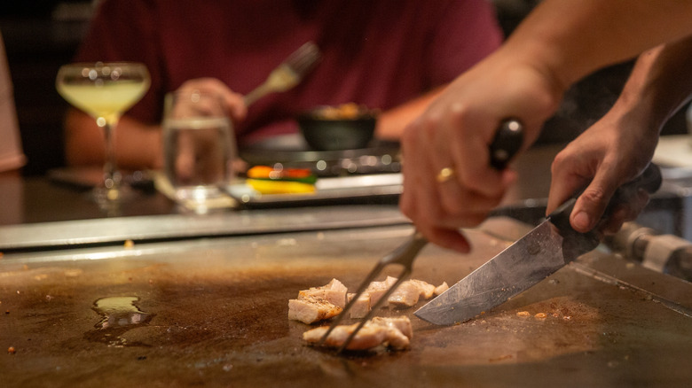 Hibachi chef preparing food on a grill with person sitting in background