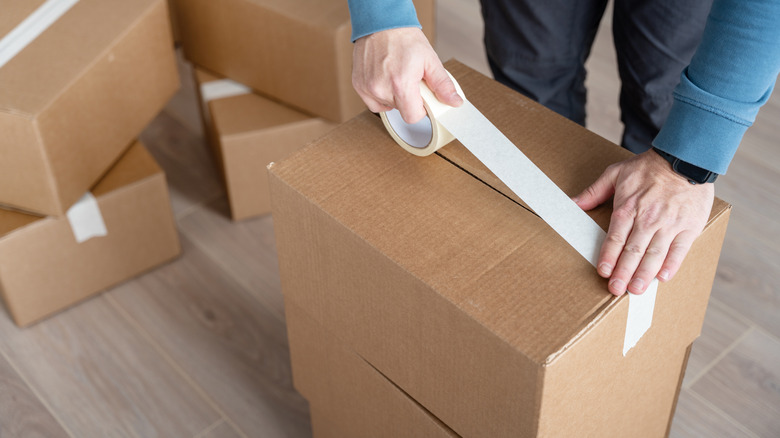 Person sealing cardboard box with white parcel tape