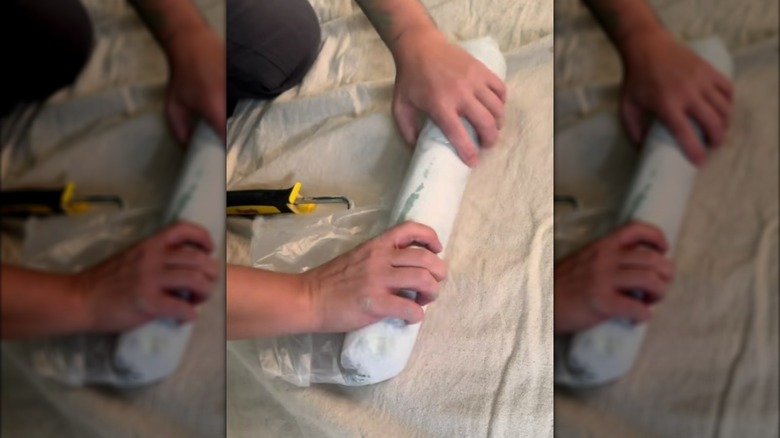Hands wrapping paint roller in plastic bag