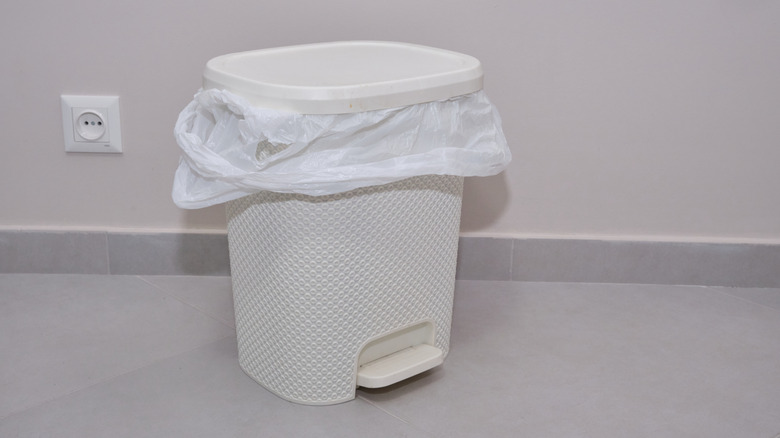 Small white pedal trash can lined with white plastic bag