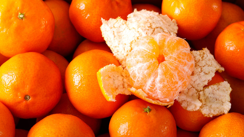 pile of clementines with a partially peeled one on top