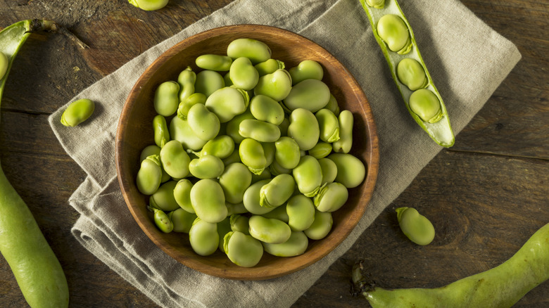 Brown bowl of green fava beans on rustic table
